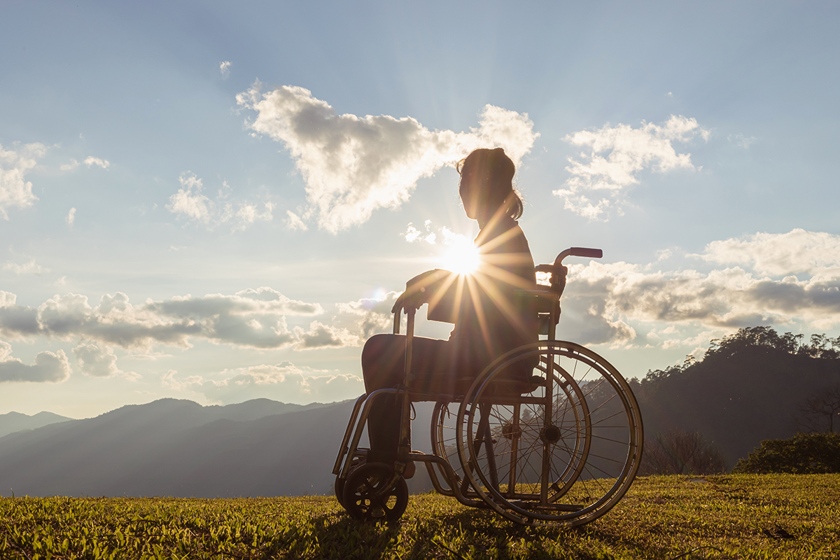 Frau im Rollstuhl sitzend auf einem Berg mit Blick in die Landschaft